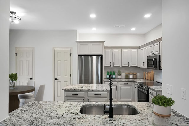 kitchen with tasteful backsplash, light stone counters, sink, and appliances with stainless steel finishes