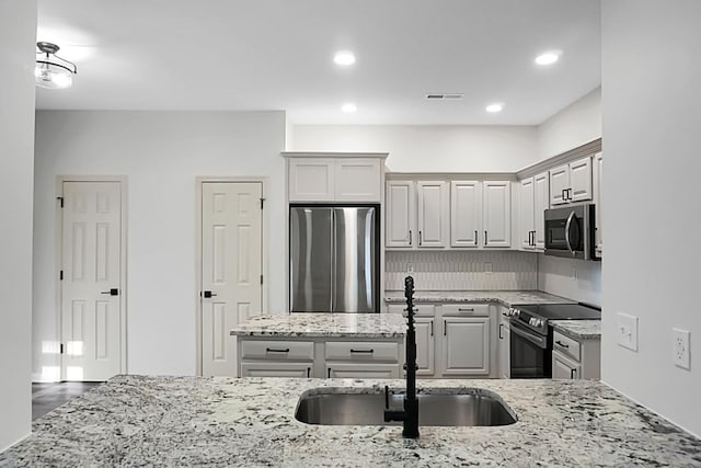 kitchen featuring backsplash, light stone countertops, sink, and stainless steel appliances