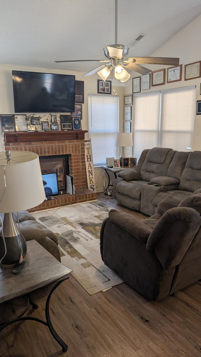 living area featuring visible vents, a brick fireplace, ceiling fan, vaulted ceiling, and wood finished floors