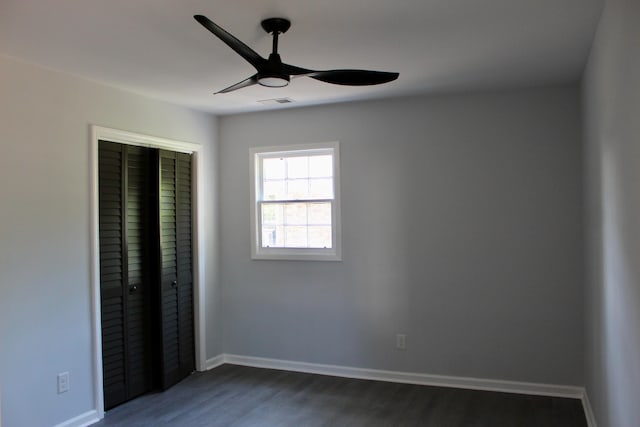 unfurnished bedroom featuring dark wood-style flooring, a ceiling fan, baseboards, visible vents, and a closet