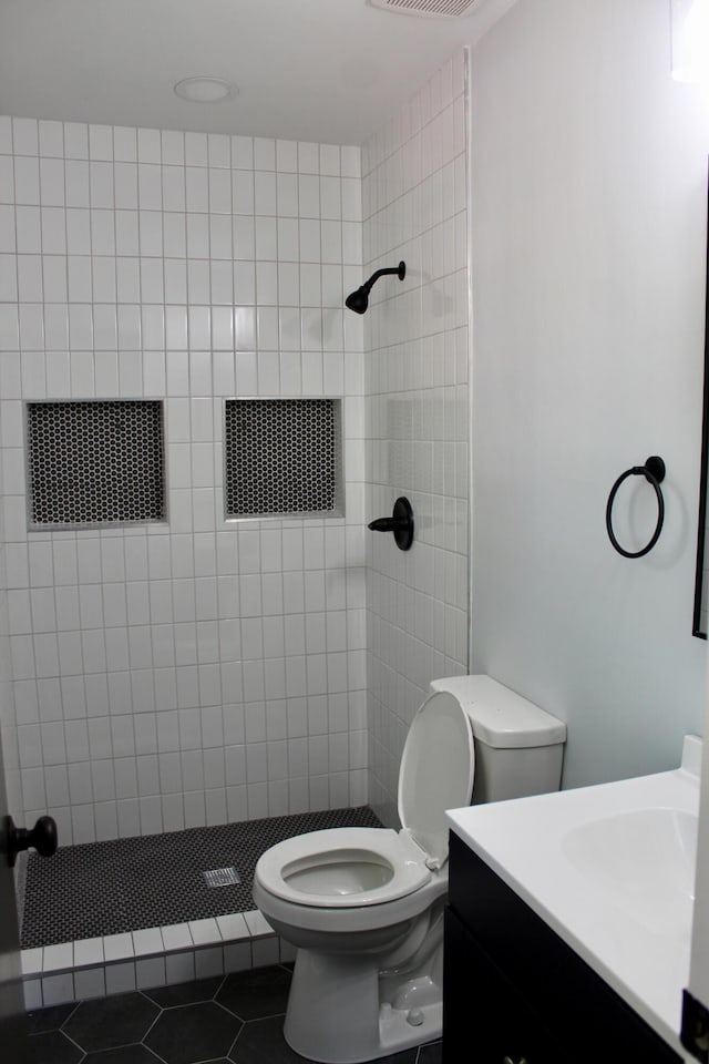 full bath featuring a tile shower, tile patterned flooring, vanity, toilet, and visible vents