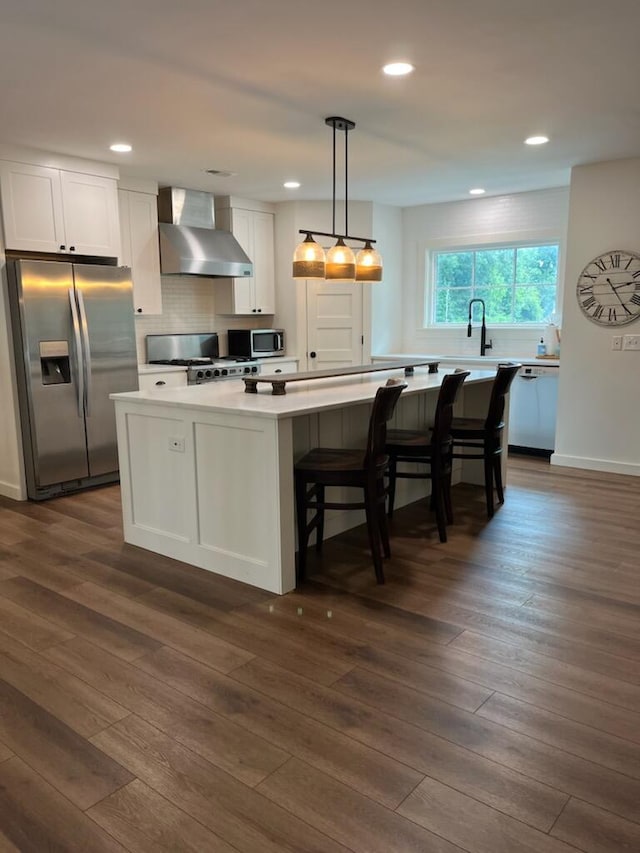 kitchen featuring a center island, dark wood-type flooring, white cabinets, wall chimney range hood, and appliances with stainless steel finishes