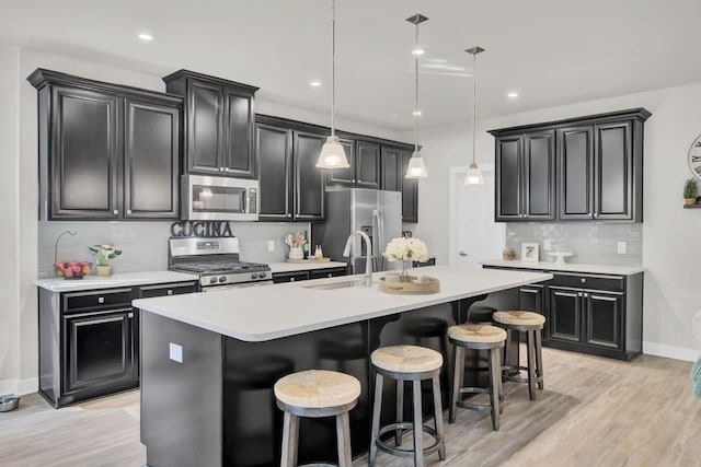 kitchen with sink, stainless steel appliances, decorative light fixtures, a breakfast bar area, and a center island with sink