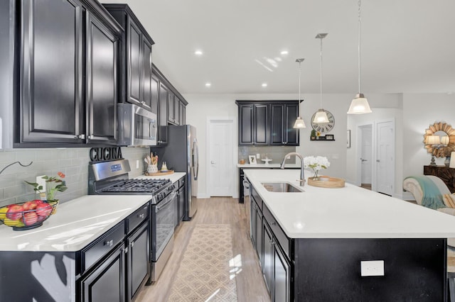 kitchen featuring appliances with stainless steel finishes, tasteful backsplash, a kitchen island with sink, sink, and decorative light fixtures