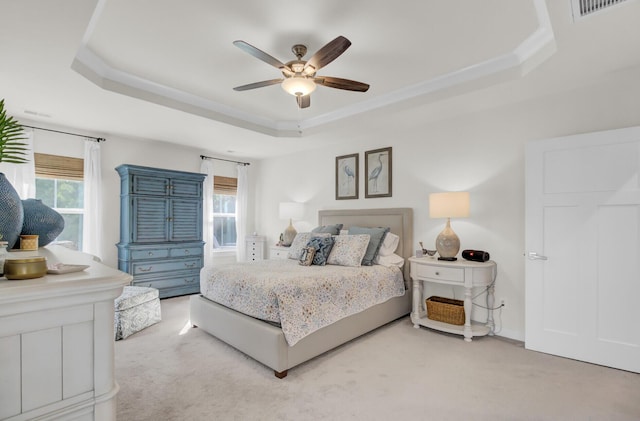 carpeted bedroom with a tray ceiling, multiple windows, and ceiling fan