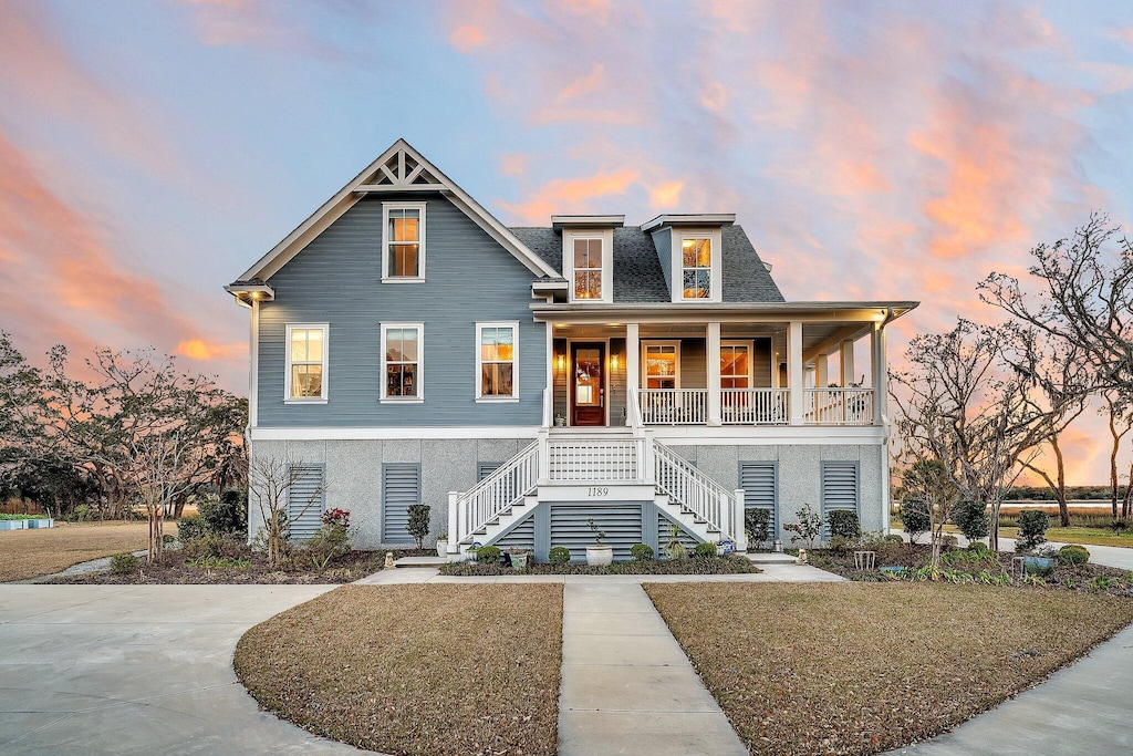 beach home with covered porch, a shingled roof, stairs, driveway, and stucco siding