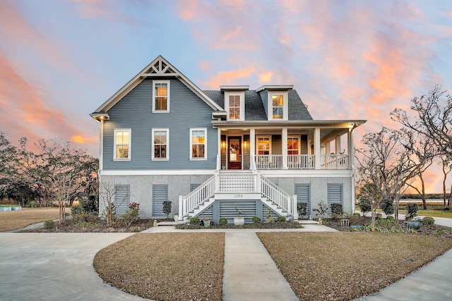 beach home with covered porch, a shingled roof, stairs, driveway, and stucco siding