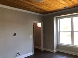 empty room with dark wood-type flooring, crown molding, wooden ceiling, and baseboards