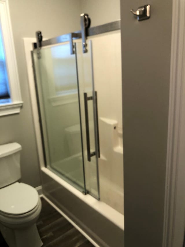 full bathroom featuring toilet, wood finished floors, and bath / shower combo with glass door