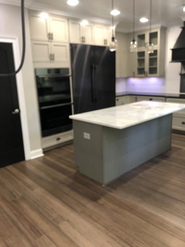 kitchen featuring freestanding refrigerator, glass insert cabinets, dark wood-type flooring, hanging light fixtures, and stainless steel double oven