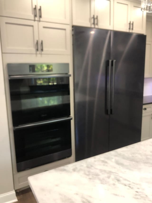 room details with double oven, high quality fridge, dark wood finished floors, baseboards, and light stone countertops