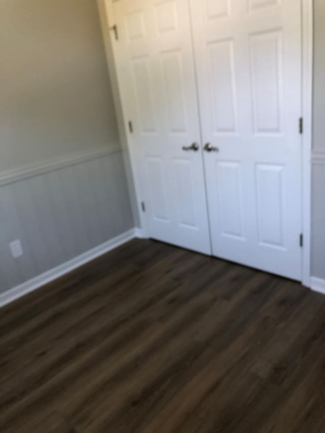 unfurnished bedroom featuring baseboards, a wainscoted wall, dark wood-style floors, and a closet