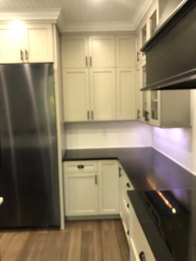 kitchen with dark wood-style floors, freestanding refrigerator, crown molding, dark countertops, and range hood