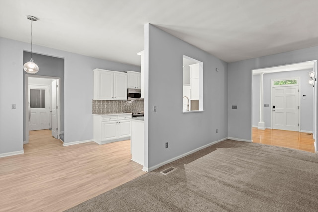 unfurnished living room featuring light wood-style floors, baseboards, a sink, and visible vents