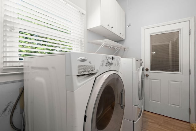 clothes washing area with light wood-type flooring, cabinet space, and washer and clothes dryer