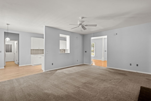 unfurnished living room with a sink, baseboards, a ceiling fan, and light colored carpet