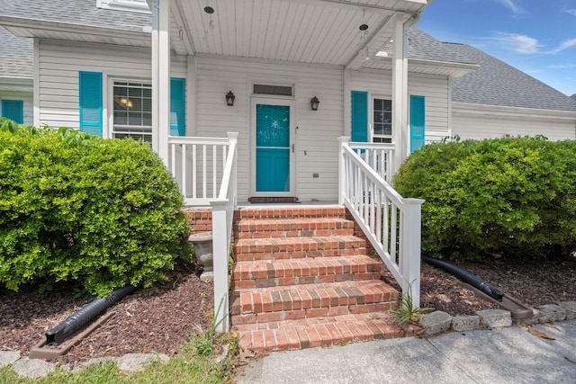 entrance to property with covered porch and a shingled roof