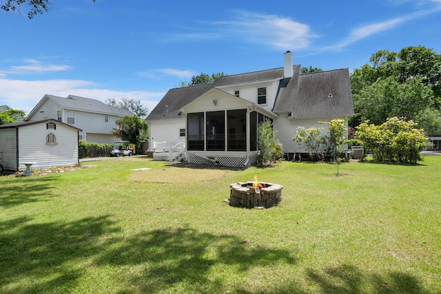 rear view of property with a lawn, a chimney, a sunroom, and an outdoor fire pit