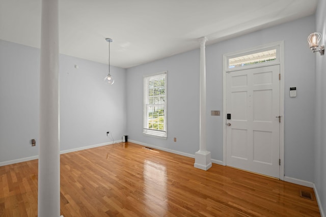 foyer entrance featuring baseboards, ornate columns, light wood-style flooring, and visible vents