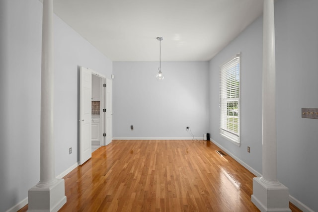 unfurnished dining area featuring ornate columns, light wood-style floors, baseboards, and visible vents