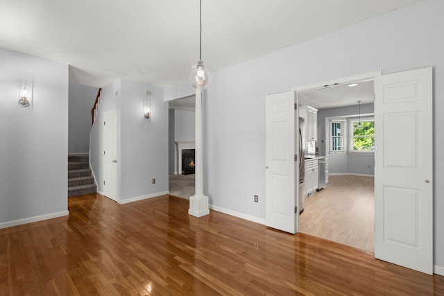 unfurnished dining area featuring baseboards, a lit fireplace, wood finished floors, and stairway