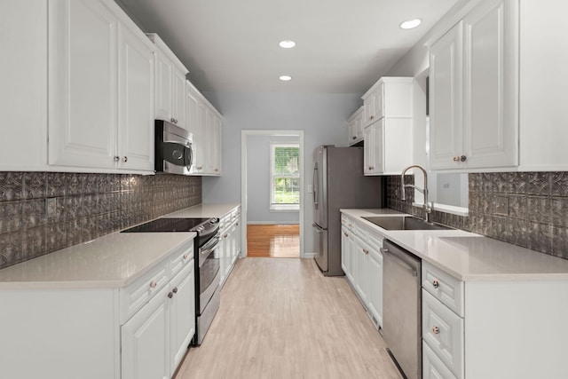 kitchen featuring a sink, appliances with stainless steel finishes, white cabinets, and light wood finished floors