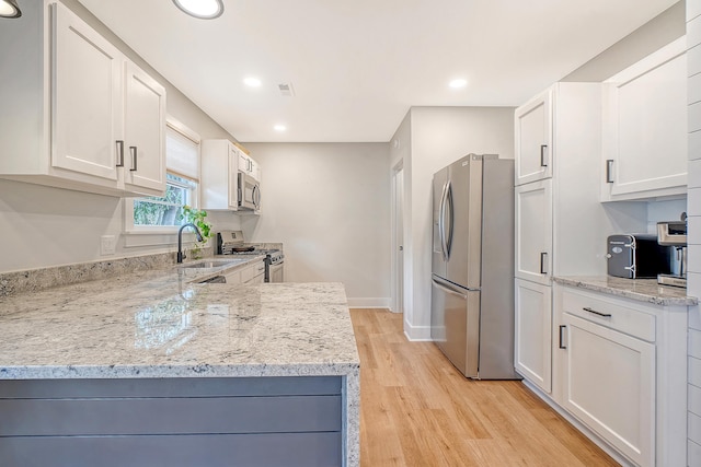 kitchen with light stone countertops, white cabinetry, appliances with stainless steel finishes, and light wood-type flooring