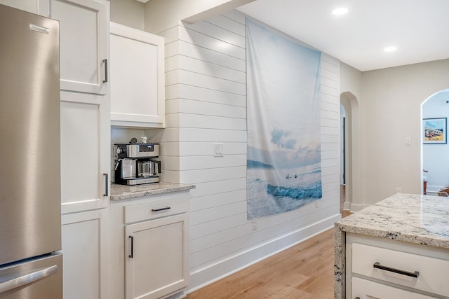 kitchen with light hardwood / wood-style flooring, stainless steel refrigerator, white cabinetry, light stone counters, and wood walls