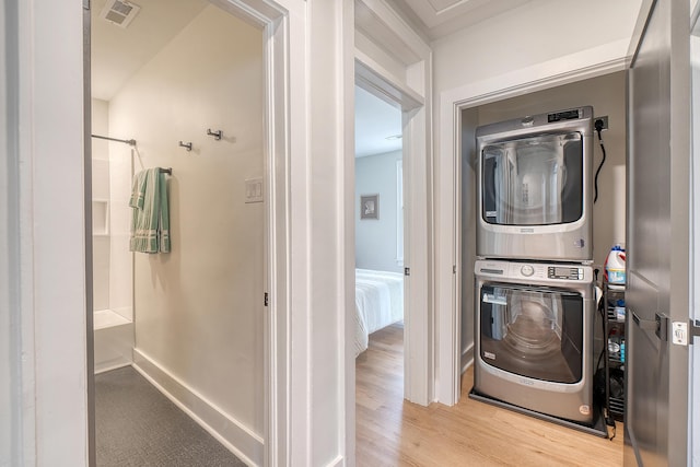 clothes washing area featuring stacked washer and clothes dryer and light hardwood / wood-style flooring