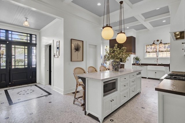 kitchen with coffered ceiling, a kitchen island, pendant lighting, white cabinetry, and stainless steel microwave