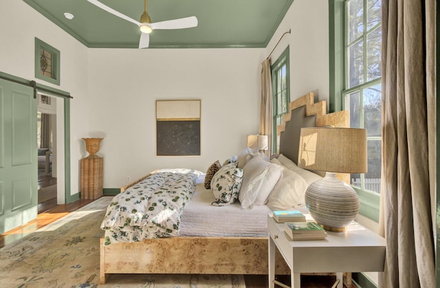 bedroom featuring a barn door, ceiling fan, crown molding, and light hardwood / wood-style floors