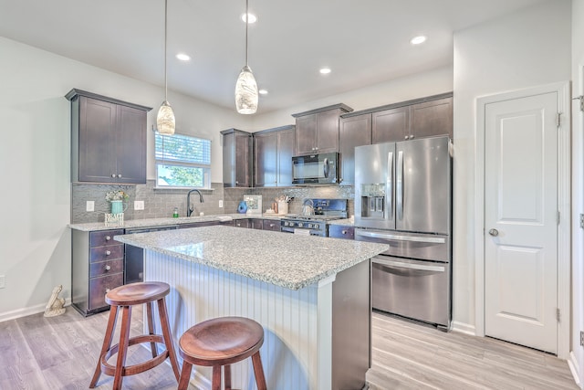 kitchen with light wood-type flooring, light stone counters, stainless steel appliances, decorative light fixtures, and a center island