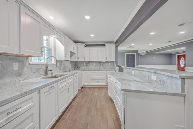 kitchen with light wood-type flooring, a sink, light stone counters, tasteful backsplash, and white cabinets