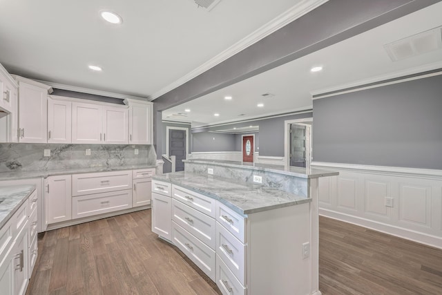 kitchen with wood finished floors, visible vents, white cabinets, wainscoting, and crown molding