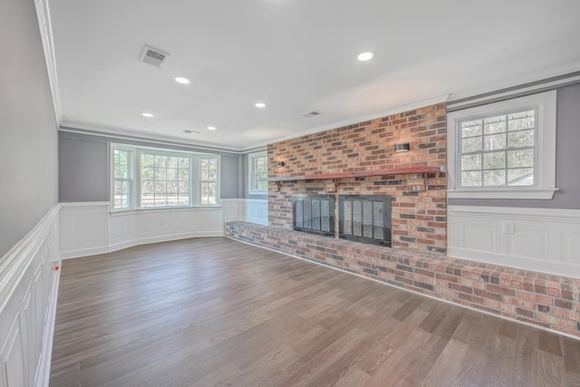 unfurnished living room with visible vents, a wainscoted wall, wood finished floors, a fireplace, and crown molding