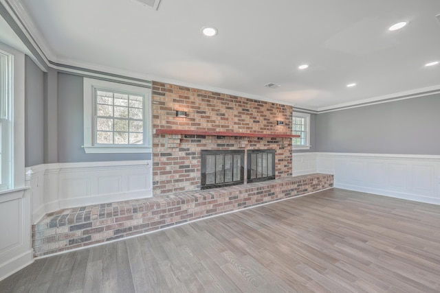 unfurnished living room featuring a wainscoted wall, wood finished floors, a brick fireplace, and ornamental molding