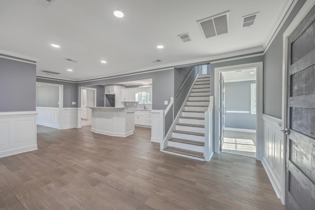 unfurnished living room featuring stairs, wood finished floors, visible vents, and ornamental molding