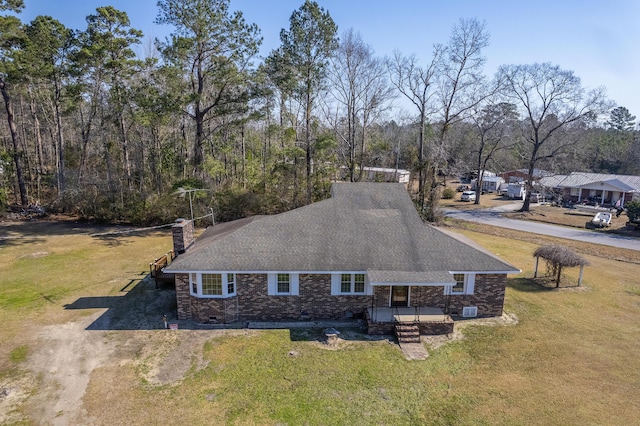 exterior space with driveway, a yard, a shingled roof, brick siding, and a chimney