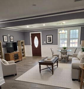 living room featuring wood finished floors, a wainscoted wall, beam ceiling, ornamental molding, and a decorative wall