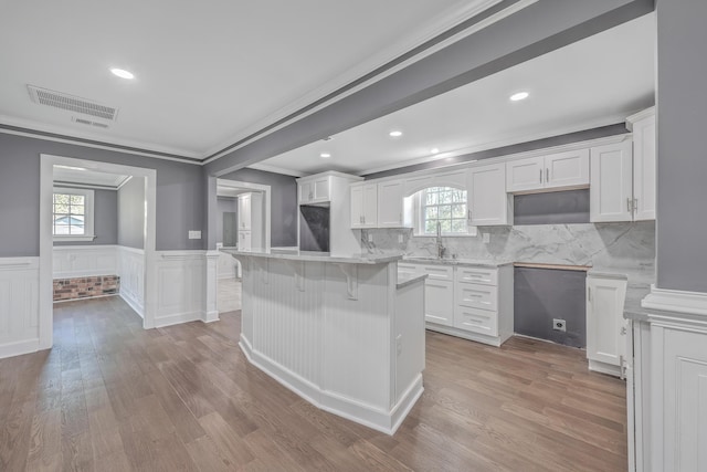 kitchen with visible vents, a sink, white cabinetry, a breakfast bar area, and wainscoting