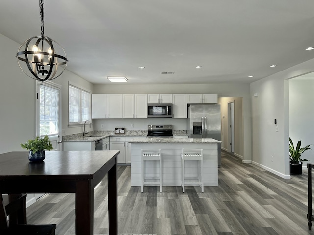 kitchen with wood finished floors, a kitchen island, a sink, stainless steel appliances, and white cabinets