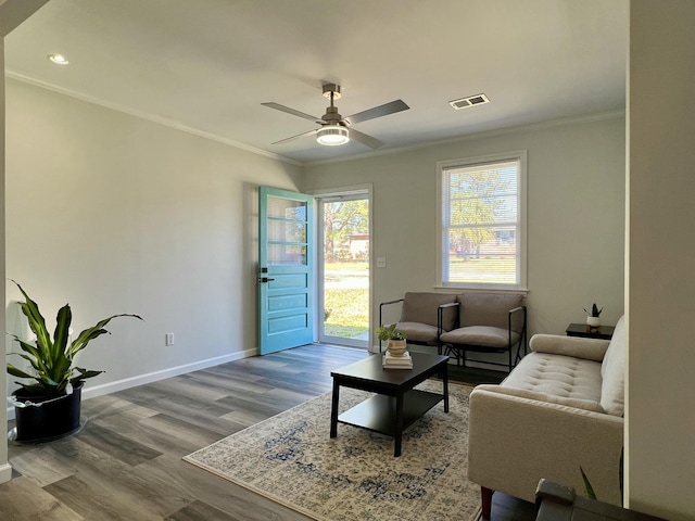 living area with wood finished floors, visible vents, baseboards, and ornamental molding