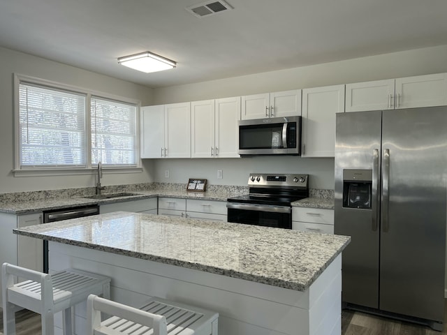 kitchen featuring visible vents, a sink, stainless steel appliances, white cabinets, and a kitchen breakfast bar