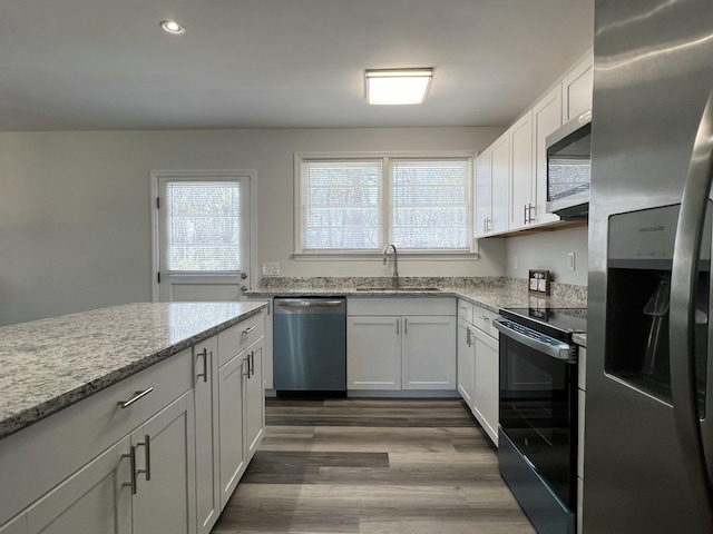 kitchen with light stone countertops, dark wood finished floors, a sink, appliances with stainless steel finishes, and white cabinetry