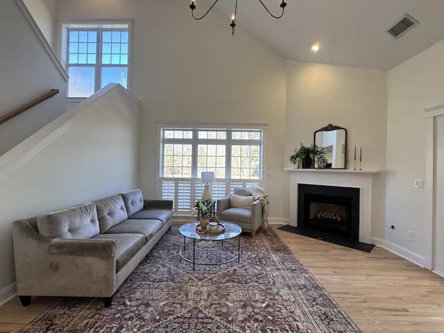 living room featuring a high ceiling, plenty of natural light, a chandelier, and light hardwood / wood-style flooring