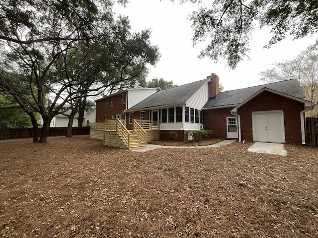 back of property featuring a deck, brick siding, fence, a sunroom, and a chimney