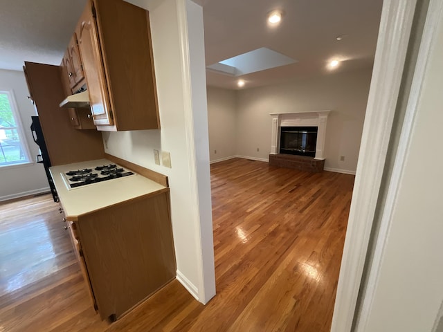 kitchen with white gas cooktop, baseboards, light wood-style floors, light countertops, and a glass covered fireplace