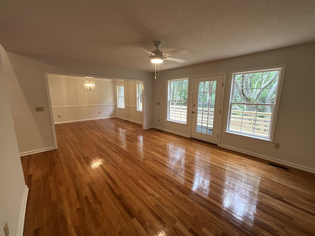 unfurnished room featuring a textured ceiling, ceiling fan with notable chandelier, wood finished floors, visible vents, and baseboards