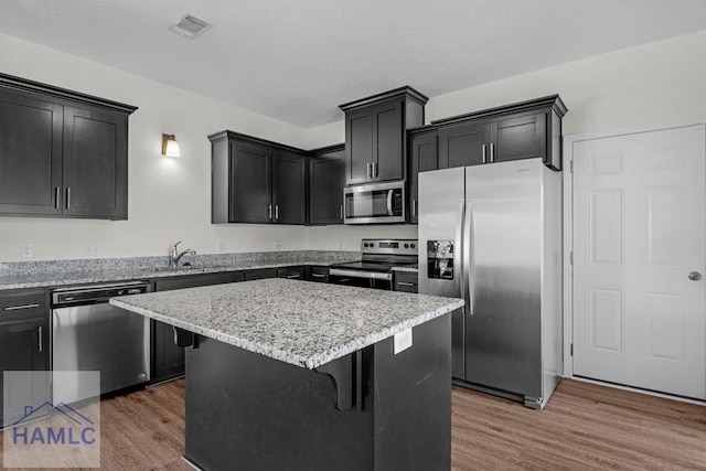 333 Grayson Ave, Hinesville, GA 31313 - kitchen featuring appliances with stainless steel finishes, wood finished floors, a kitchen island, dark cabinets, and a kitchen breakfast bar