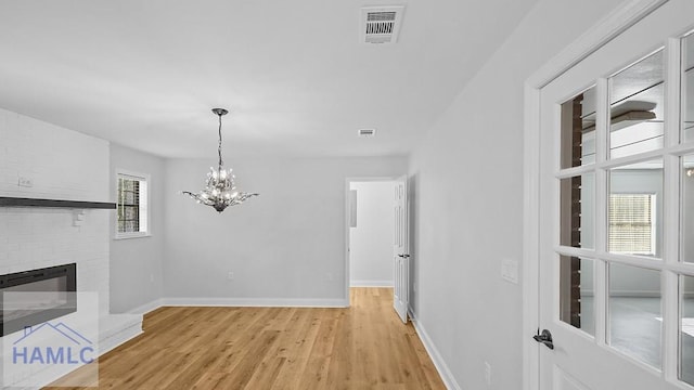 unfurnished living room featuring a chandelier, light hardwood / wood-style flooring, a brick fireplace, and a wealth of natural light